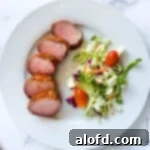 Sun-Kissed Suppers Made Simple 15 Elegant slices of smoked pork tenderloin served on a white dinner plate, accompanied by a fresh side salad.