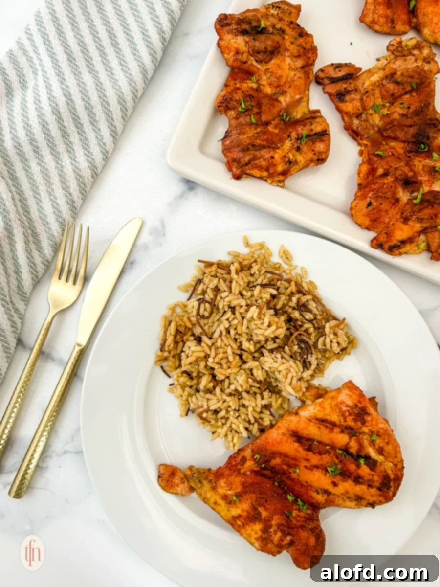 Sun-Kissed Suppers Made Simple 5 Perfectly smoked chicken thigh with a side of rice on a white plate, accompanied by a larger platter of chicken in the background.