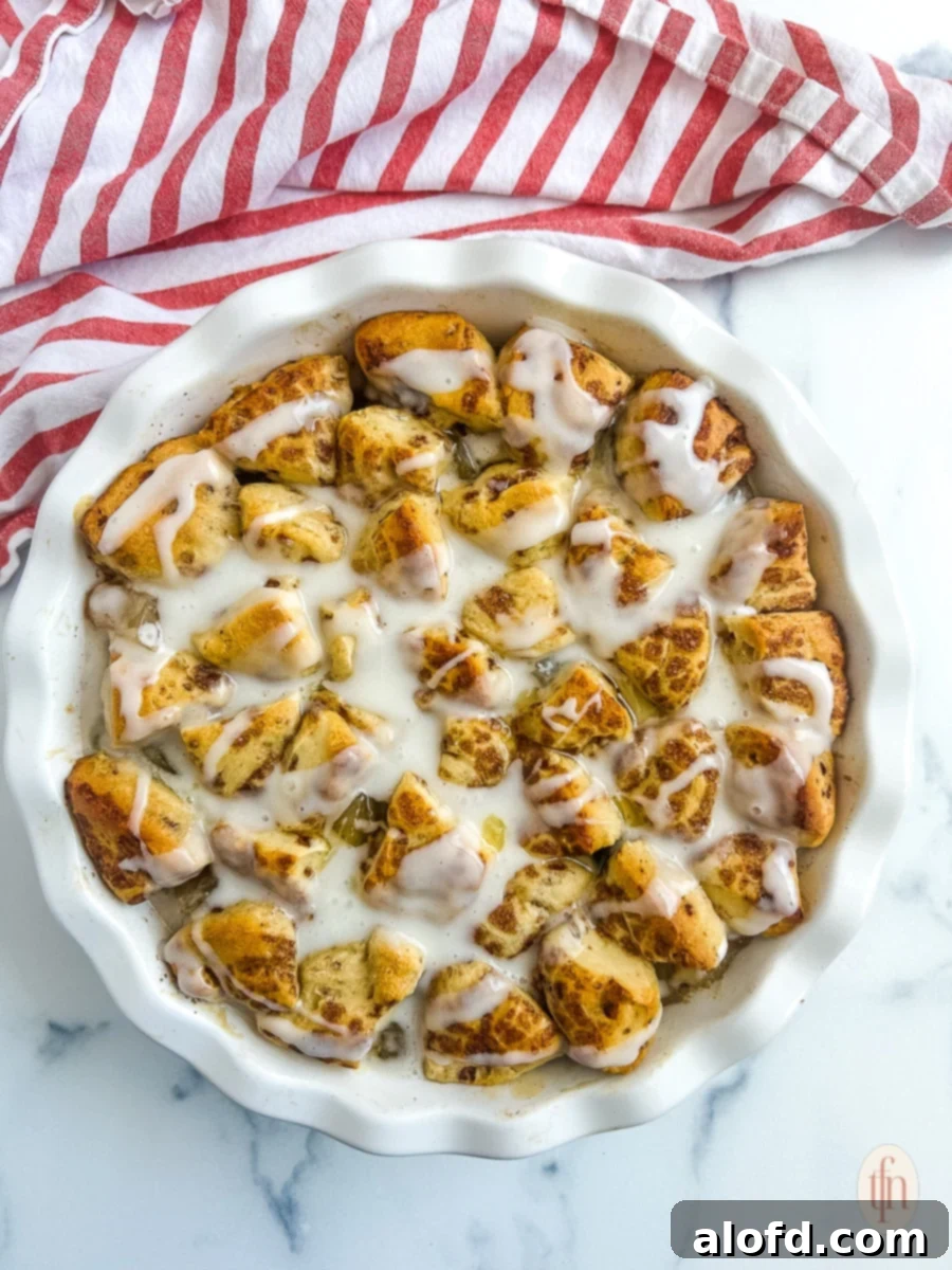 Cinnamon rolls with apple pie filling in a white dish on a white marble background, showcasing a perfect golden bake.