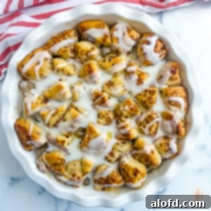 Cinnamon rolls with apple pie filling in a white dish on a white marble background.