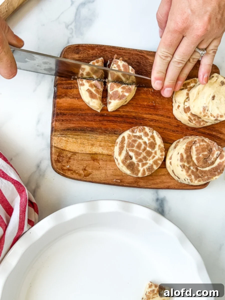 Cutting cinnamon roll rounds into fourths with a knife on a cutting board, preparing them for the apple bake.