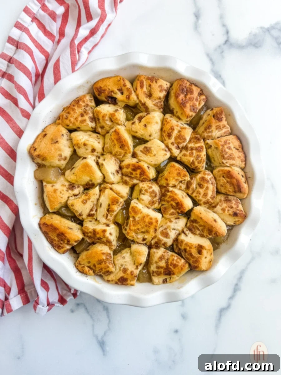 Baked cinnamon rolls with apple pie filling in a white dish, fresh out of the oven, on a white background.