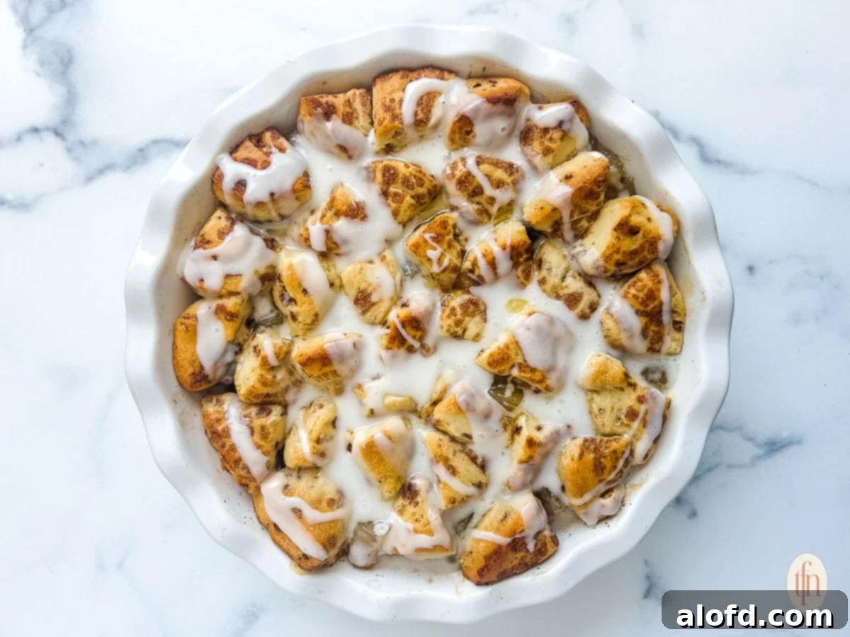 Cinnamon rolls with apple pie filling in a white dish on a white marble background, ready to be enjoyed.