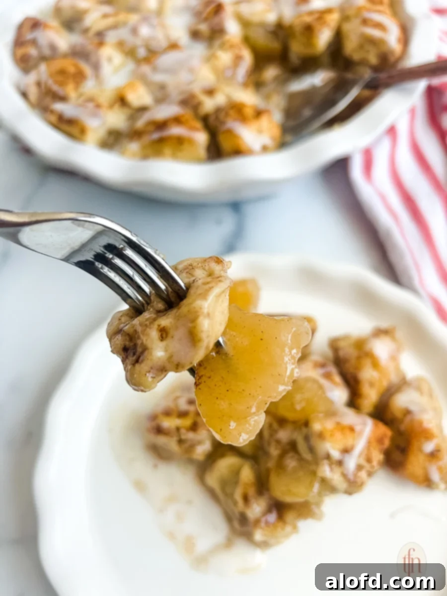 Closeup of warm, gooey cinnamon rolls on a fork over a white plate, showing the delicious apple filling.