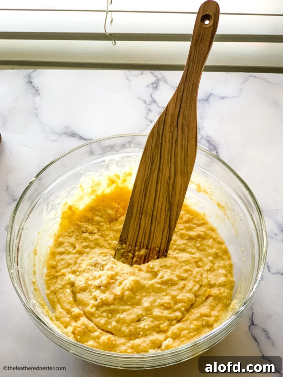 Bisquick Cornbread No Cornmeal Needed 5 Wood mixing spoon in a bowl of quick bread batter, showing a well-combined and smooth consistency.