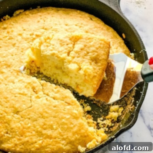 Bisquick Cornbread No Cornmeal Needed 8 Slice of Bisquick corn bread on a spatula above cast iron skillet, golden brown and fluffy.