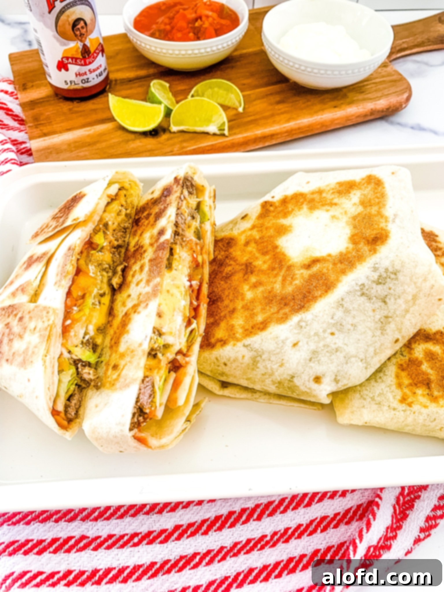 Blackstone Dinners Made Simple 3 A white platter of Blackstone Crunchwrap tortillas cut in half on top of a red and white napkin, with a bowl of salsa and slices of limes in the background, illustrating a vibrant griddle meal.