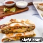 Blackstone Dinners Made Simple 6 Copycat crunchwrap cut in half, displayed on a serving board with bowls of sour cream, salsa, a bottle of Tapatio, and fresh lime slices in the background.