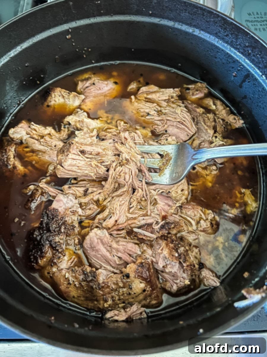 Fork in a pot of Dutch oven carnitas.