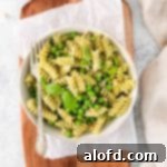 Lunchbox Hacks for Educators 17 A fork piercing into a generous serving bowl of pesto pasta with assorted vegetables, beautifully garnished with fresh basil.