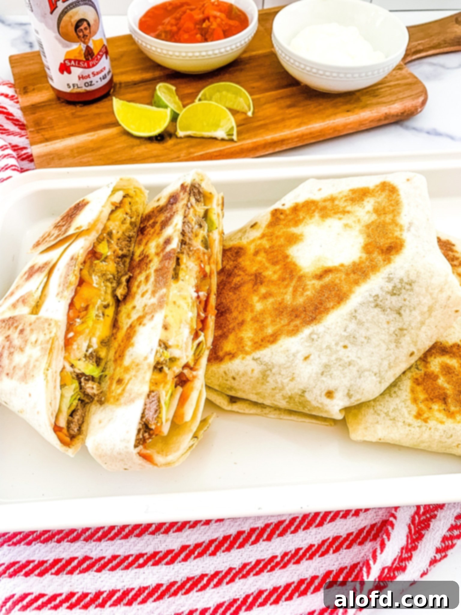 Lunchbox Hacks for Educators 19 A white platter adorned with Blackstone Crunchwrap tortillas, cut in half and resting on a vibrant red and white napkin. A bowl of salsa and lime slices are artfully arranged in the background.