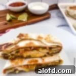 Lunchbox Hacks for Educators 20 A delectable copycat crunchwrap, perfectly cut in half, displayed on a serving board. Bowls of sour cream, salsa, a bottle of Tapatio, and fresh lime slices are arranged invitingly in the background.