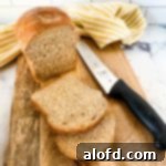 Harvest Bowls and Loaves 26 sliced whole wheat sandwich bread on a bread board with a knife and yellow and white kitchen towel and bread knife.