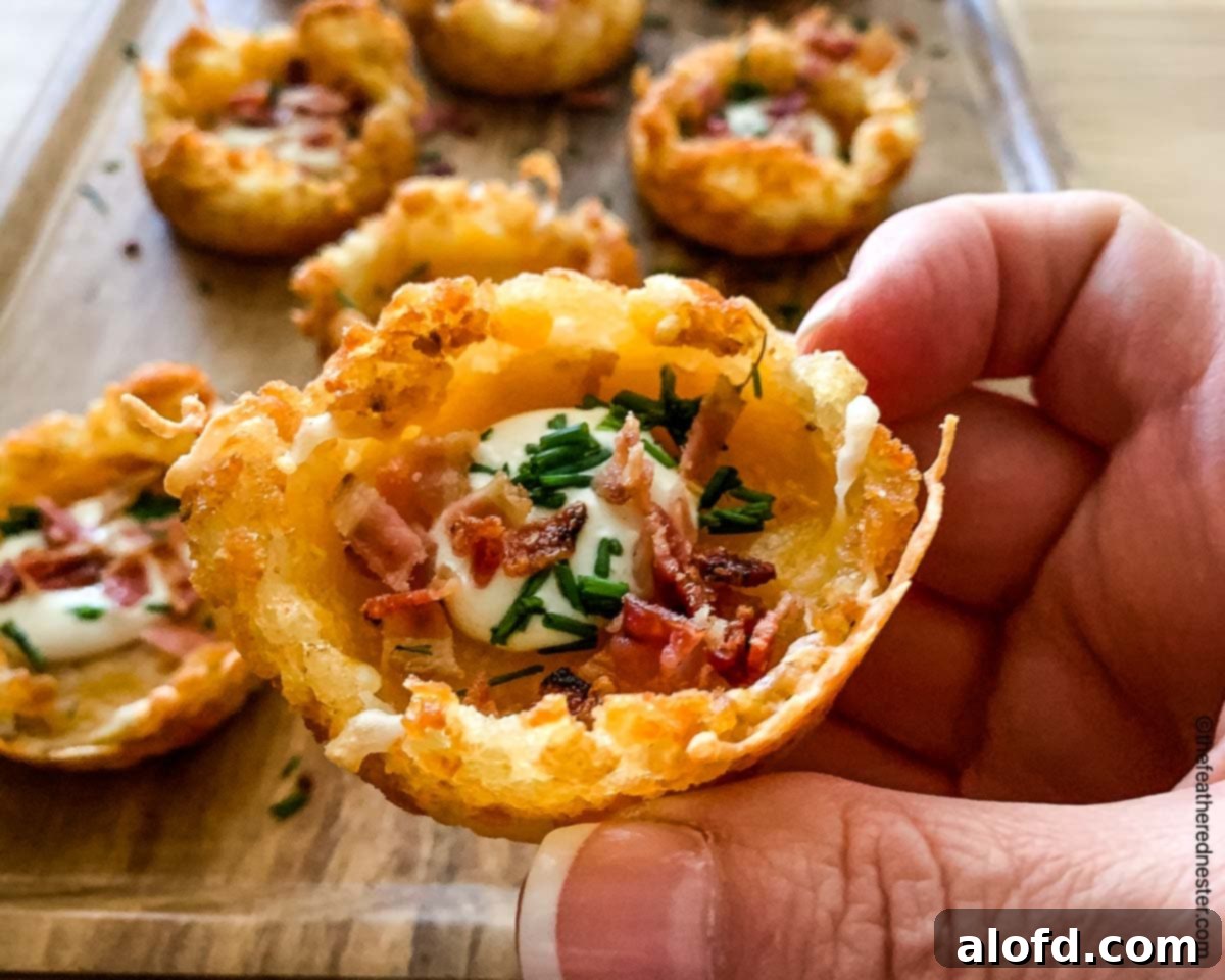 a hand holding a tater tots appetizer up close with more in the background on a wooden platter.