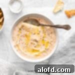 roasted red pepper feta dip in a white bowl with spoon above it and placed in a parchment paper and a striped cloth, bowl of pita chips and salt in the background.