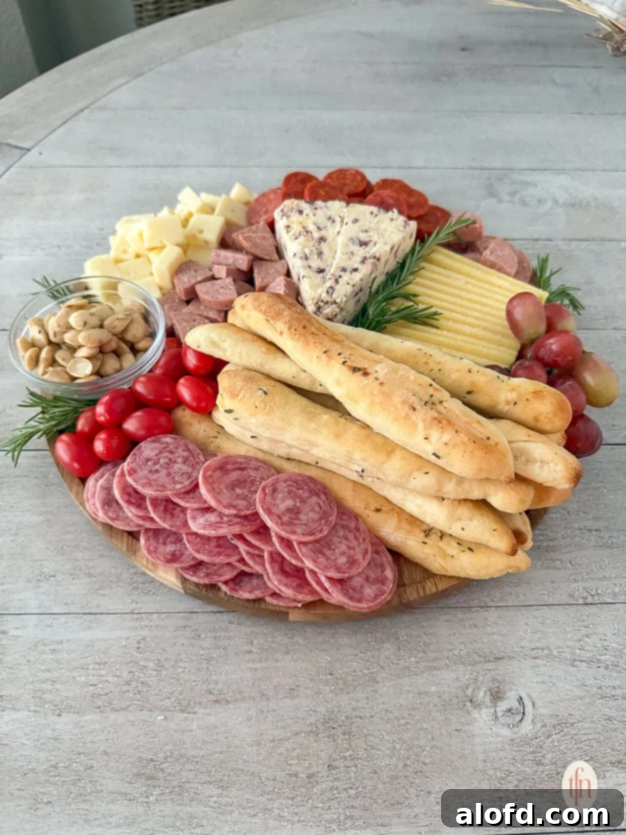 A round charcuterie board mixed with bread, meat, tomatoes, fruits, and cheese.