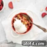 Game Day Grub 38 a white ramekin of apple strawberry cobbler with vanilla ice cream on top, and a spoon ready to serve it.
