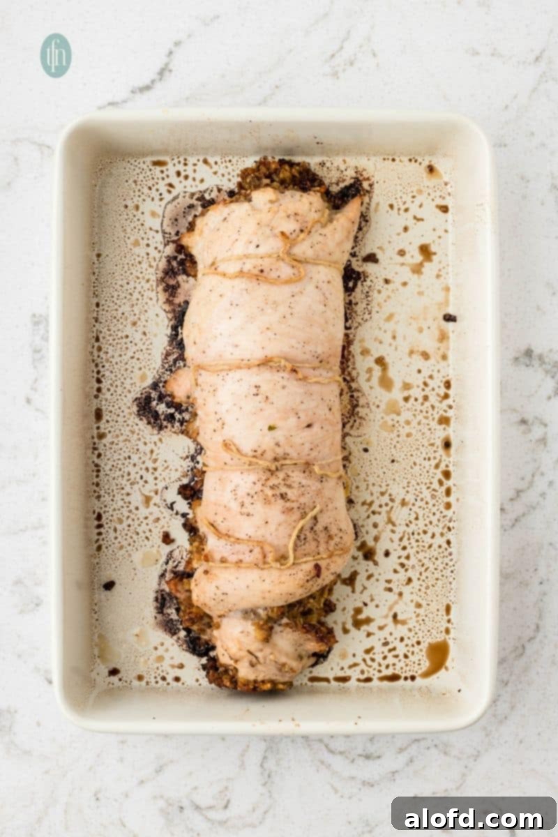 The golden-brown, roasted stuffed turkey breast, tied with twine, resting on a cutting board after baking.