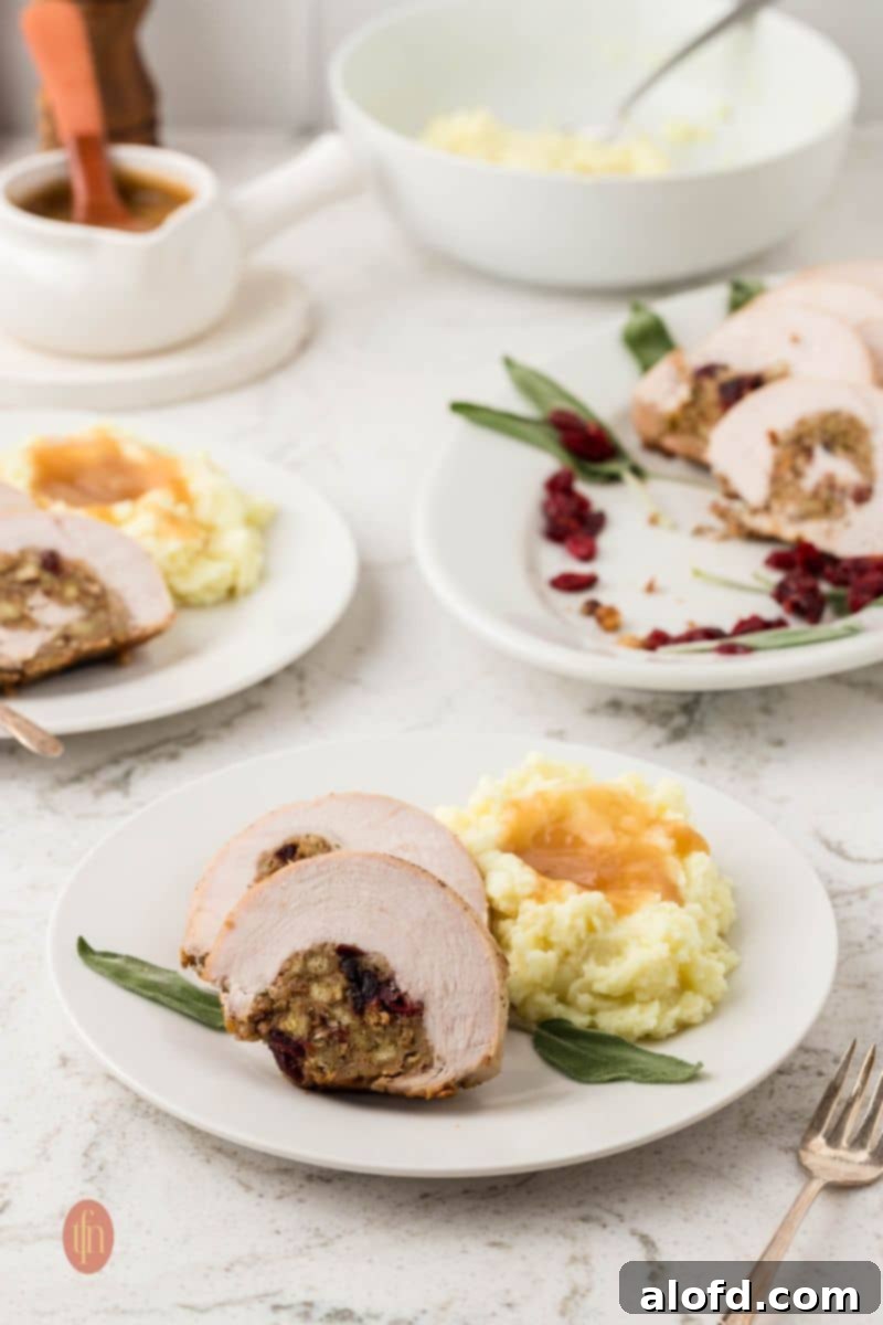 A low-angle shot showing three plates of food on a marble counter. The foreground plate holds two slices of stuffed turkey breast and mashed potatoes with gravy. A gravy boat and a bowl of mashed potatoes are in the background.