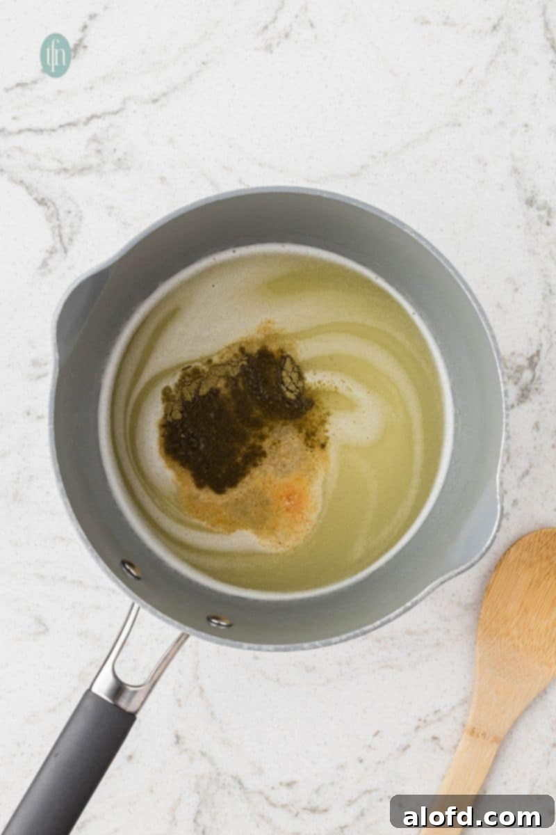 An overhead shot of a saucepan containing a light liquid, likely broth or melted butter, with a mound of dark seasoning and spices ready to be mixed for the stuffing.