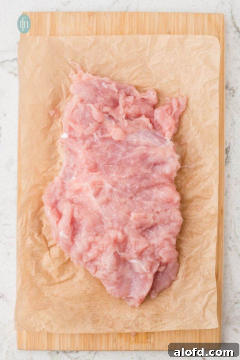 An overhead shot of a raw turkey breast tenderloin that has been butterflied and pounded flat, resting on parchment paper on a cutting board.