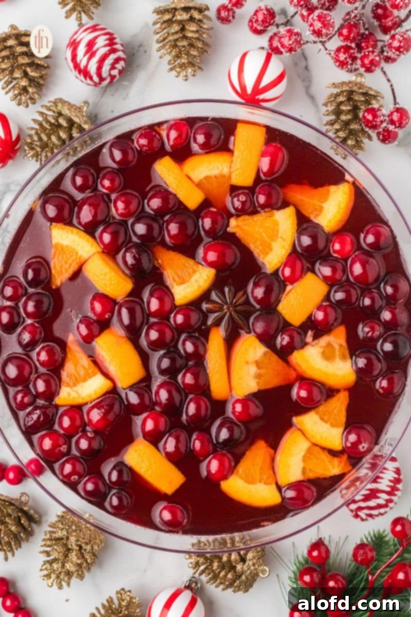A beautiful non-alcoholic Christmas punch in a glass bowl, floating with bright red cranberries, orange slices, and a whole star of anise.