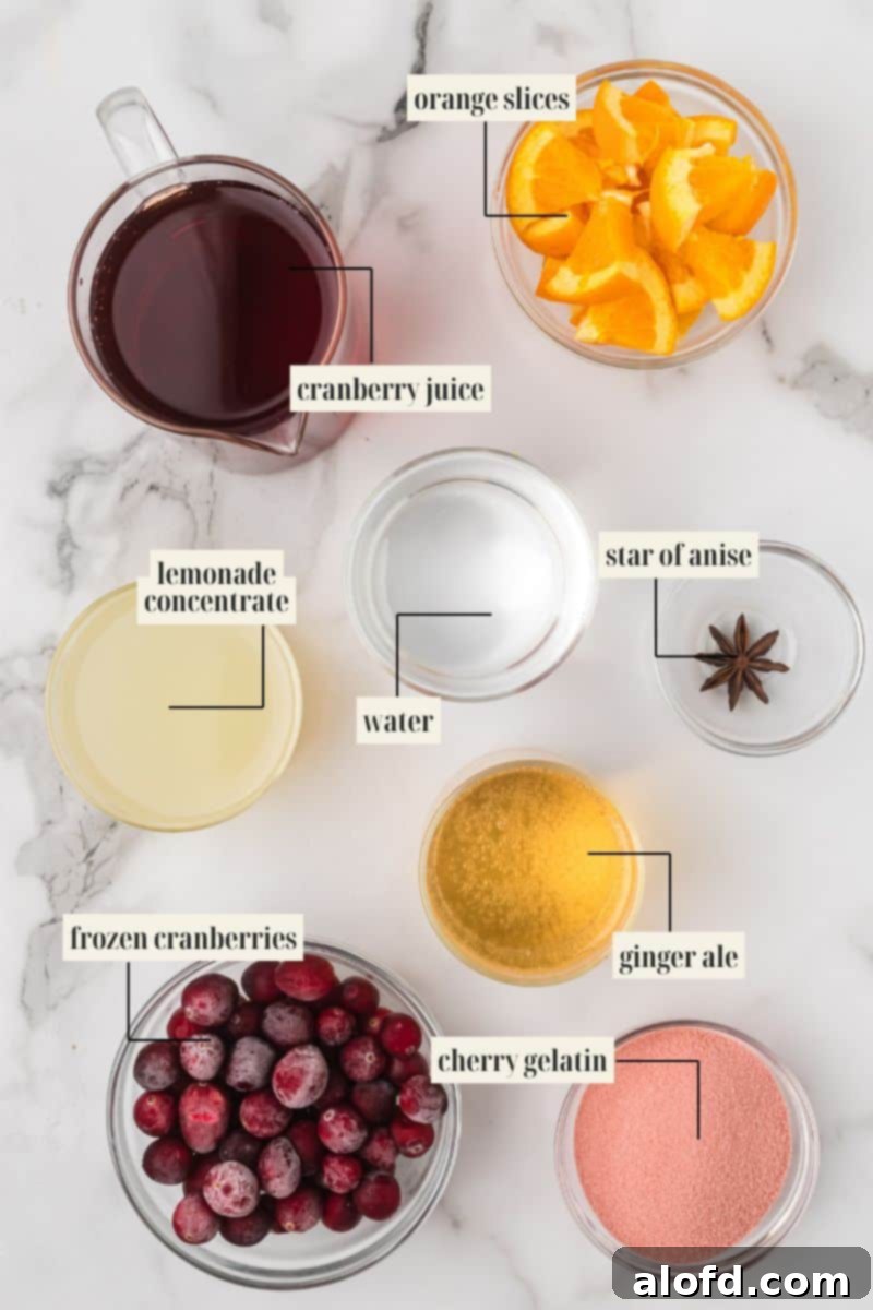 Flat lay photo of ingredients for holiday punch: a pitcher of cranberry juice, bowls of orange slices, frozen cranberries, lemonade concentrate, water, ginger ale, cherry gelatin mix, and a star of anise.