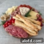 A beautifully arranged round charcuterie board, featuring a delightful mix of bread, savory meats, fresh tomatoes, vibrant fruits, and an assortment of cheeses.