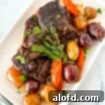 A square photograph of a pristine white serving plate generously laden with Dutch Oven Pot Roast and a colorful array of accompanying vegetables.
