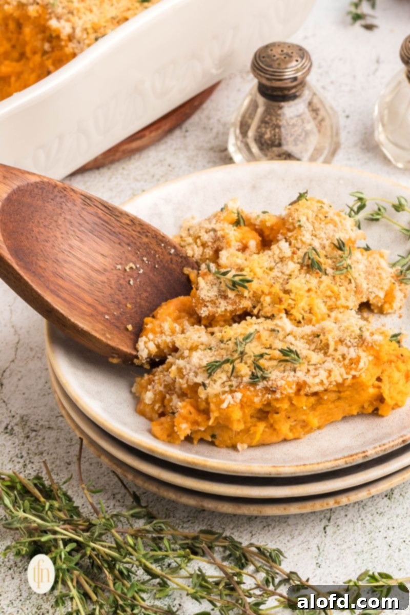 A generous scoop of savory sweet potato casserole, artfully placed on a stack of pristine plates, with a wooden spoon resting nearby.