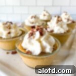 A square photograph displaying six individual cups of creamy pumpkin custard, each elegantly topped with a dollop of whipped cream and a sprinkle of nuts.