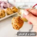 A skewered meatball, expertly made with this delicious sausage ball recipe, with a tray of pimento cheese balls visibly in the background.