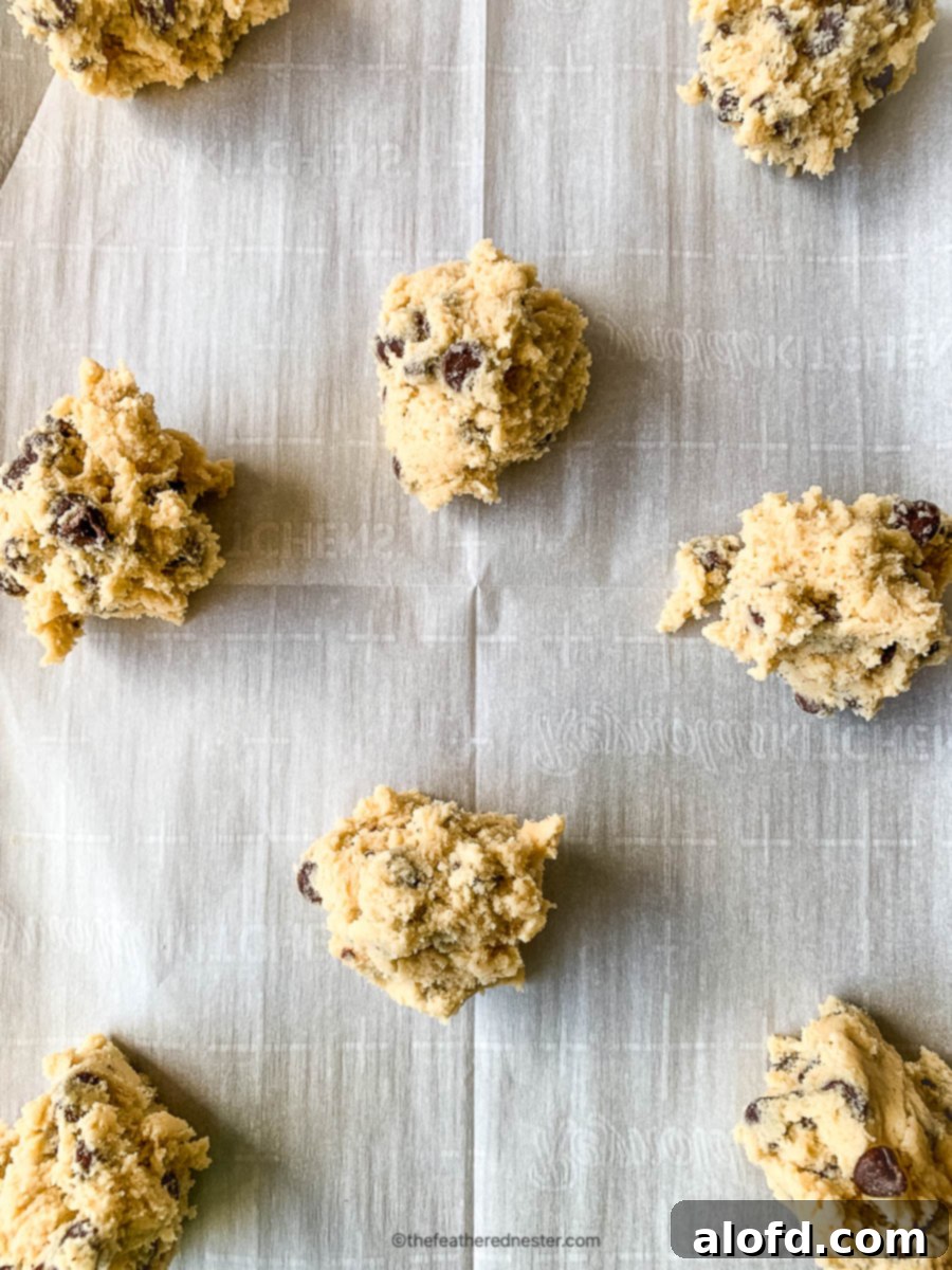 Raw scoops of eggless cookie dough arranged on a parchment-lined cookie sheet, ready for baking.