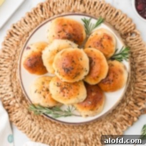 A plate of cheese stuffed dinner rolls stacked with rosemary sprigs for garnish with a bowl of cranberries and butter for serving.