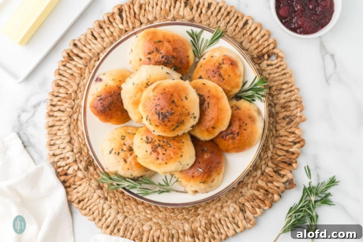 A beautifully arranged plate of baked stuffed bread rolls, garnished with rosemary sprigs and accompanied by a bowl of cranberry sauce and butter.
