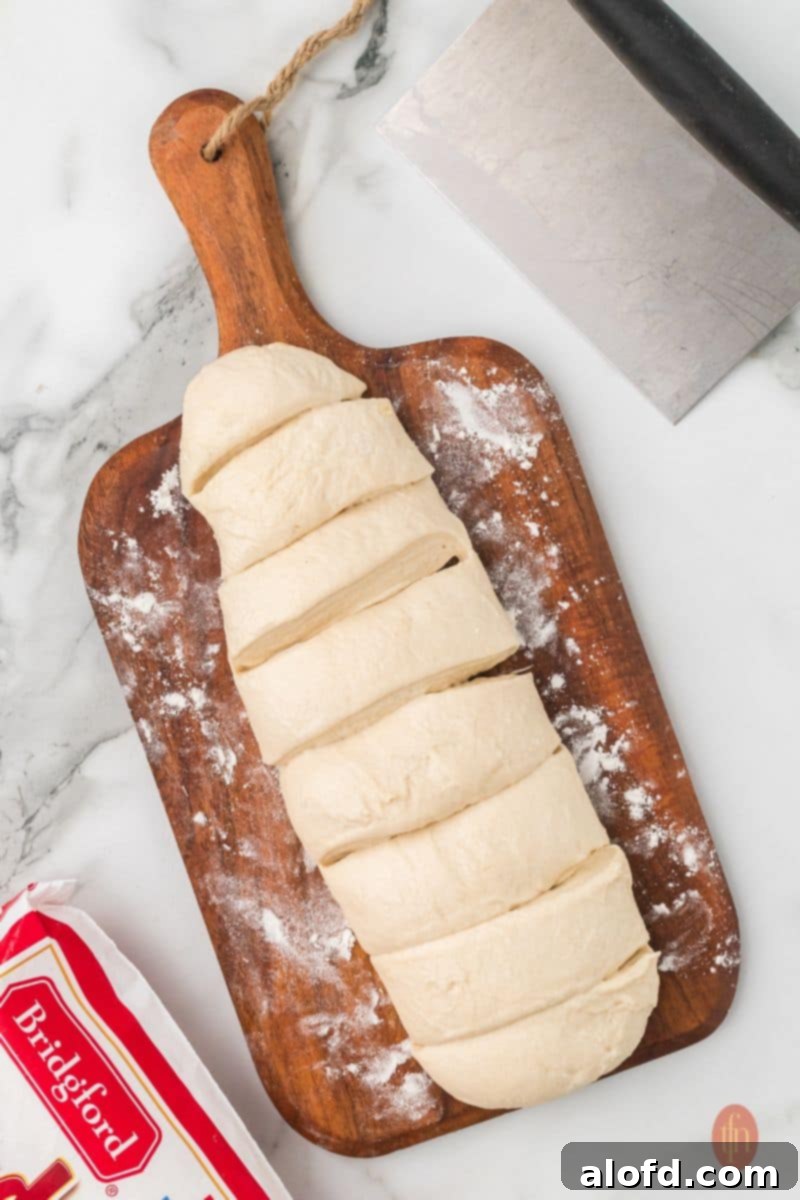 A loaf of thawed bread dough, sliced and ready to be used, resting on a wooden cutting board.