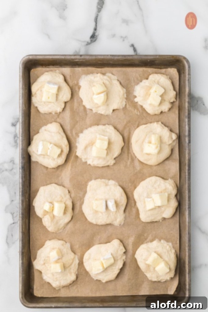 A baking sheet of dough and cheese, showing the preparation stages of the cheese stuffed dinner rolls.