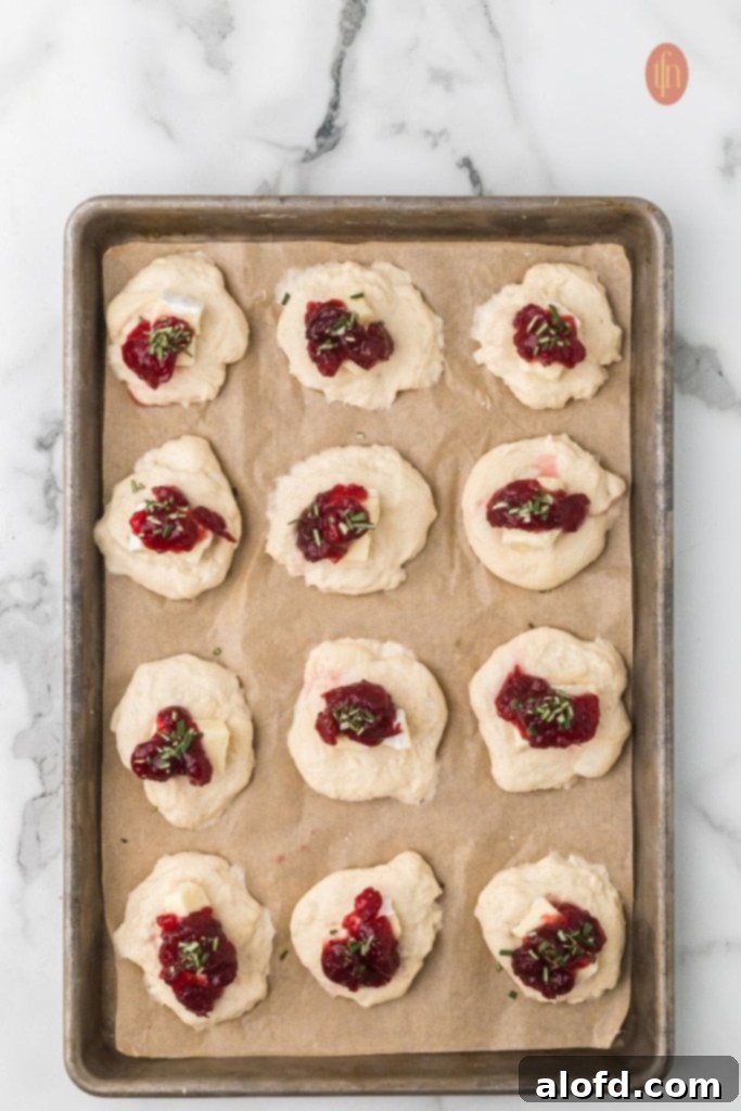 A baking sheet of dough circles filled with brie and cranberry sauce, ready to be sealed.