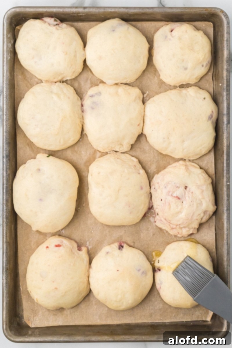 Brushing the risen rolls with melted butter before baking.