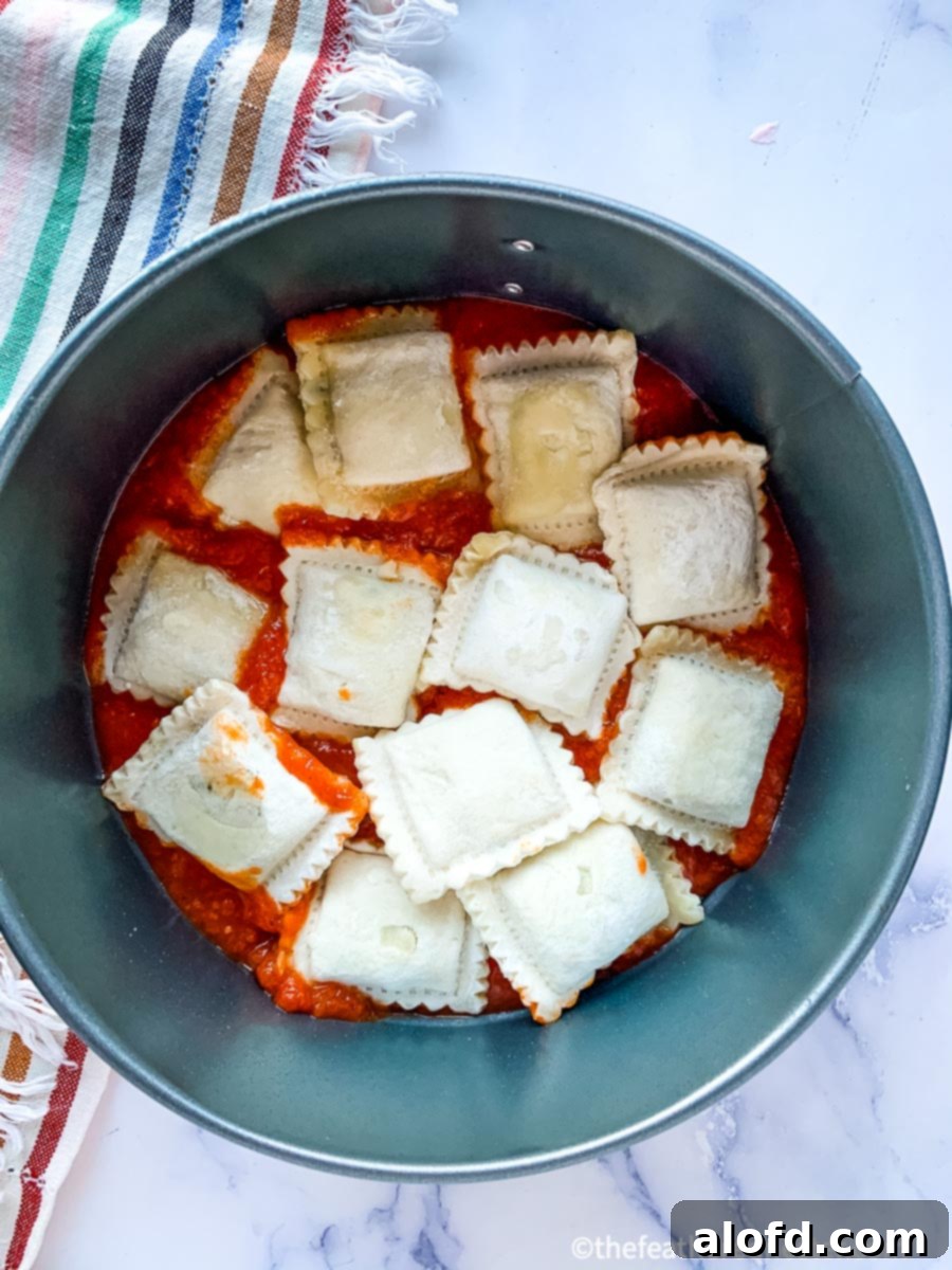 Frozen ravioli layered with sauce in a round springform pan, ready for the Instant Pot.