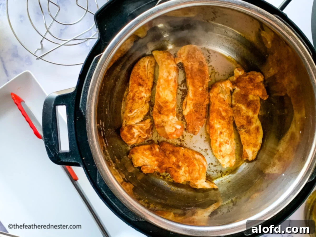 Sautéed chicken tenderloins developing a golden color inside a pressure cooker, preparing for the next step of the cooking process.
