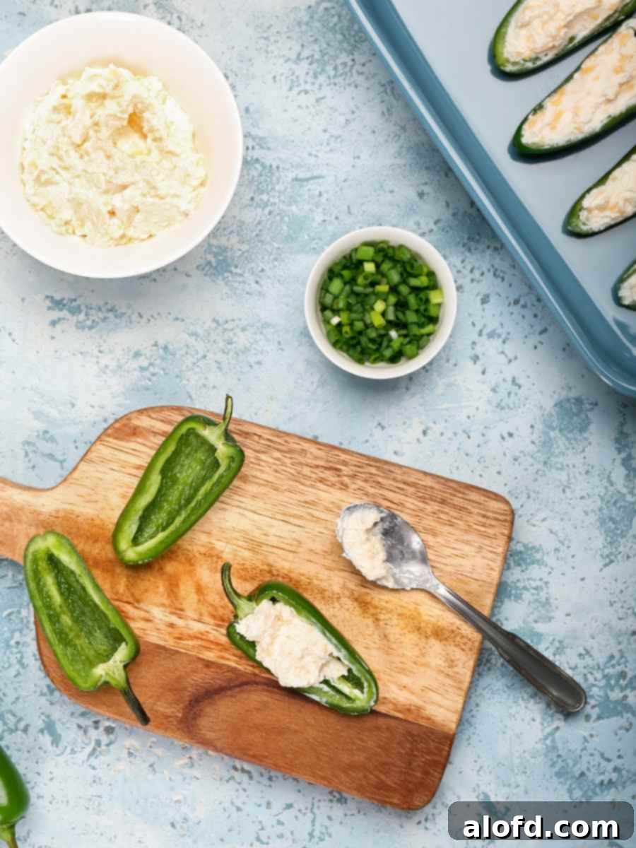 Ultimate Jalapeno Poppers 5 Close-up of a hand stuffing jalapeno peppers with cream cheese mixture.
