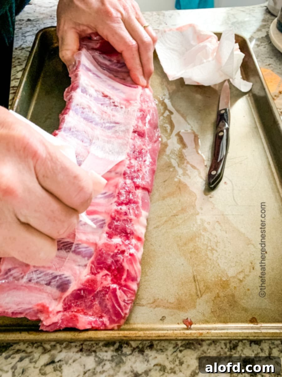 a baking sheet with a rack of baby back ribs, the membranes are being stripped from the rib bones