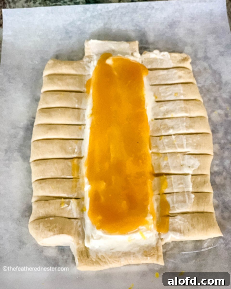 Dough with lemon curd and cream cheese spread down the middle and 1-inch strips cut down the sides, prepared for braiding.
