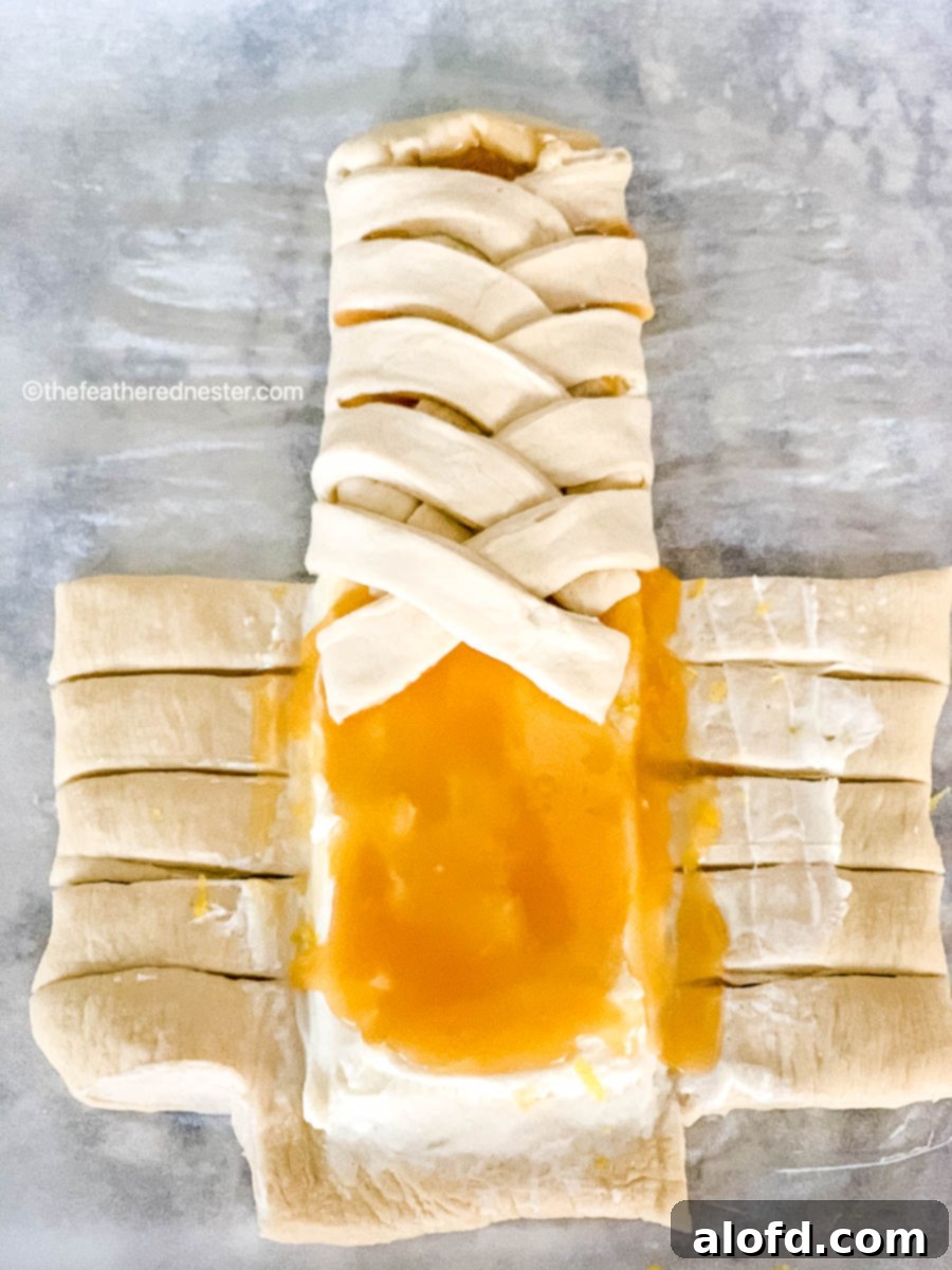 Dough with lemon curd and cream cheese spread down the middle, with strips already being braided in a crisscross pattern.