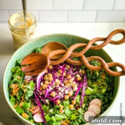 Green bowl of salad with a blend of kale and romaine salad with a jar of tahini dressing in the background.