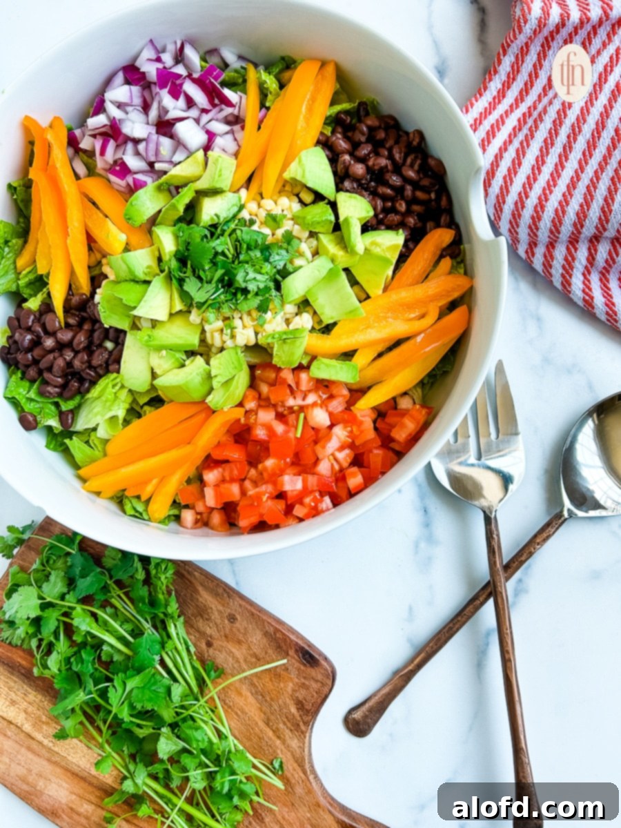 Vibrant Tex Mex salad featuring avocado, colorful bell peppers, corn kernels, red onion, cilantro, black beans, and diced tomatoes.