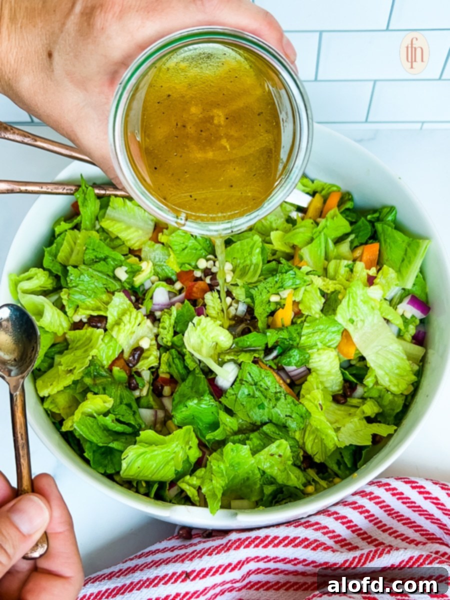 Pouring vinaigrette dressing over a Tex Mex salad with fresh vegetables and beans.