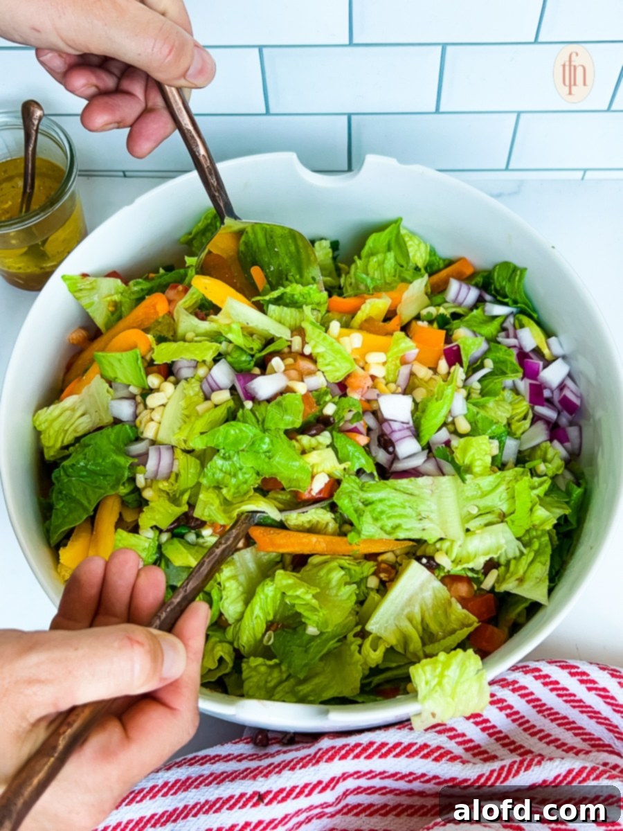 Tossing romaine lettuce, chopped vegetables, and dressing in a large serving bowl, preparing the cowboy salad.