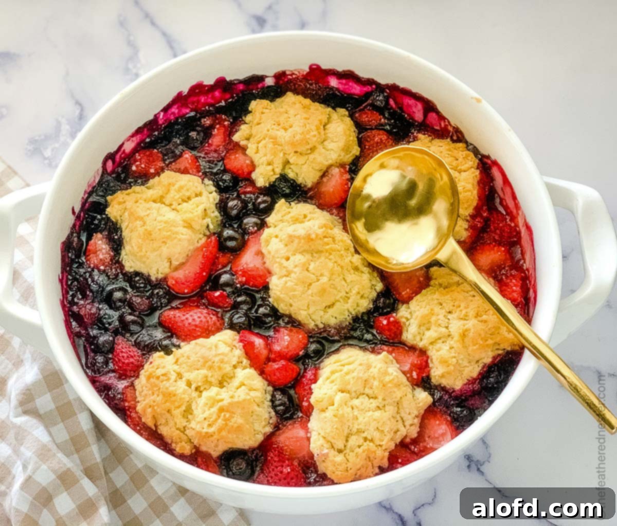 Strawberry blueberry cobbler on a white dish with spoon. 